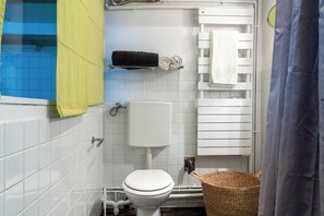 Un baño con inodoro, un lavamanos blanco, una bañera blanca, un perchero blanco y una cesta de mimbre.