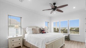 A bedroom with a large bed, a nightstand, a dresser, a ceiling fan, and large windows. - Heated Pool Hot Tub Gulf View Elevator, Top (Gulf Shores)