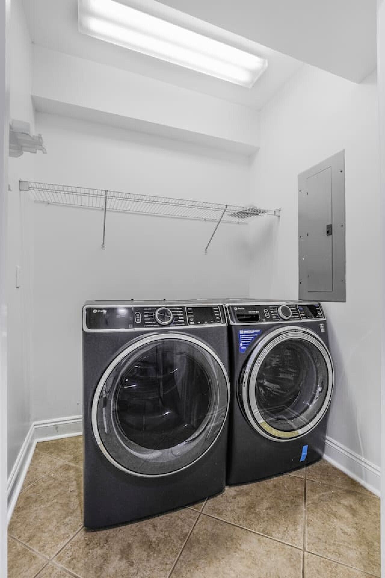 A laundry room with two front-loading washing machines, a metal drying rack, and a light fixture on the ceiling.