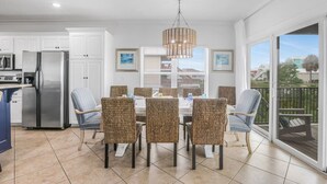 A modern kitchen with white cabinets, a stainless steel refrigerator, and a dining area with wicker chairs and a chandelier. - Private Heated Pool Hot Tub Gulf View Elevator (Gulf Shores)