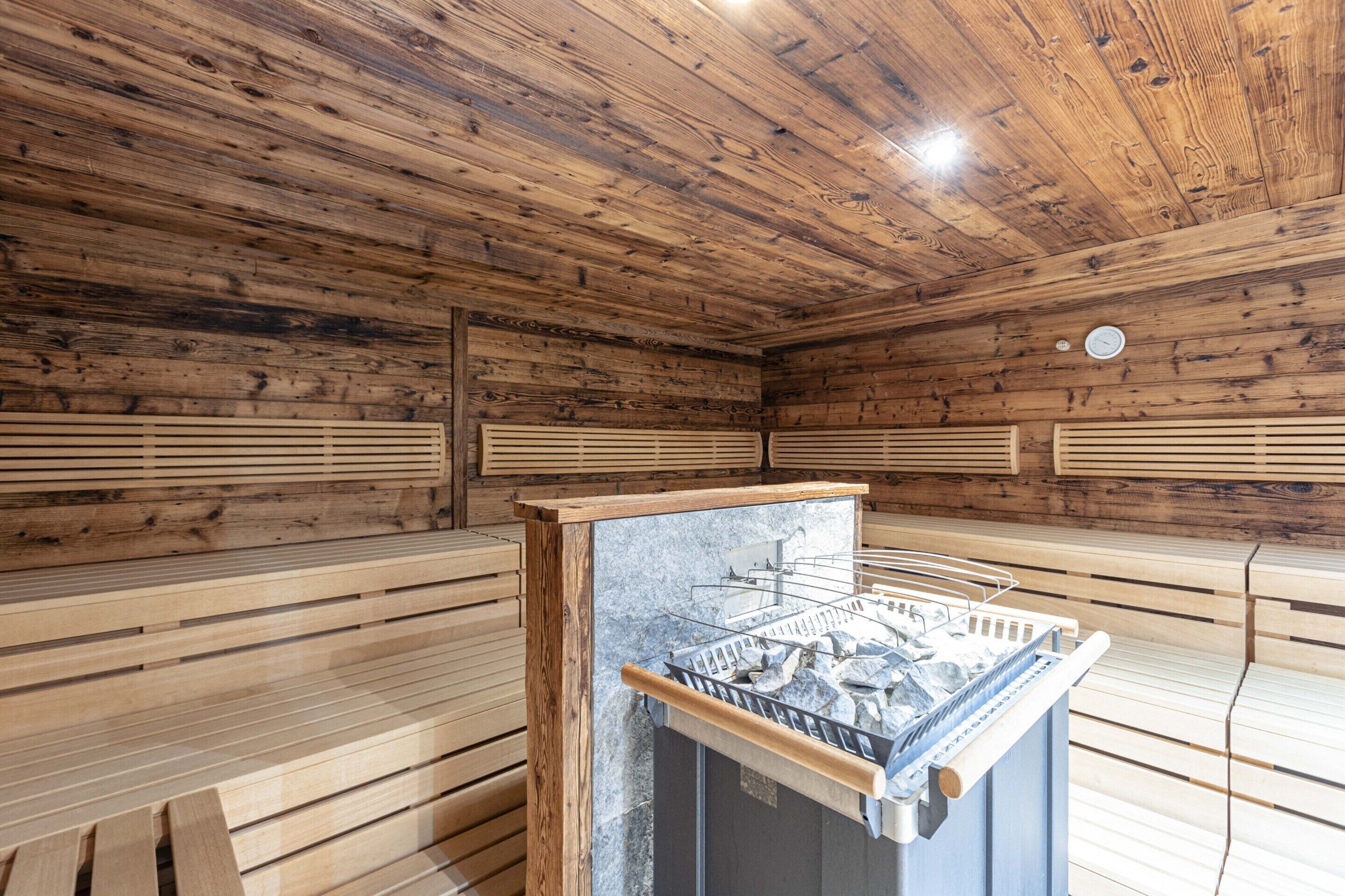 A sauna room with wooden walls and benches, a sauna machine, and a clock on the wall.