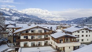 A snow-covered mountain village with chalet-style buildings, a clear sky, and a mountain range in the background.