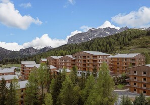 A cluster of wooden buildings with multiple floors and balconies, surrounded by dense forest and mountains in the background. - Nice Lodge With Balcony (Hermagor-Pressegger See)