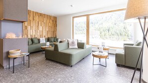 Una sala de estar moderna con chimenea, sofás verdes y un amplio ventanal con vistas a un bosque.