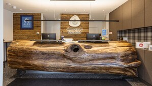 Una mesa de recepción con cubierta de madera grande, dos portátiles y un cartel que dice "Almresort Nassfeld".