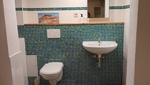 A bathroom with a white toilet, a sink with a green tiled backsplash, and a small cabinet. - Beautiful vacation room near Wutachschlucht (Löffingen)