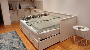 A bedroom with a bed, a small table, a nightstand, a dresser, a kitchen area, and a window. - Beautiful vacation room near Wutachschlucht (Löffingen)