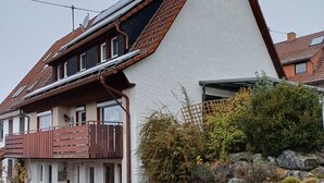 A two-story house with a sloped roof, a balcony, and a stone wall with plants. - Beautiful vacation room near Wutachschlucht (Löffingen)