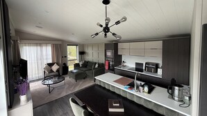 A modern kitchen with a central island, built-in appliances, and a dining area with a dark wood table and chairs. - Malton 2-bed Lodge, Sleeps 4, Pet Friendly (Malton)