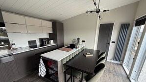 A modern kitchen with a central island, a dining area with a dark table, and a ceiling fan. - Malton 2-bed Lodge, Sleeps 4, Pet Friendly (Malton)
