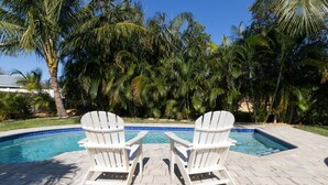 A swimming pool with two Adirondack chairs facing it, surrounded by palm trees. - *NEW* Riverside Retreat w/ Pool (Jupiter)