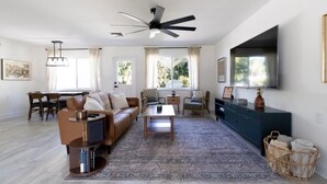 A spacious living room with a sofa, coffee table, and TV. There is a dining area with chairs and a table. - *NEW* Riverside Retreat w/ Pool (Jupiter)