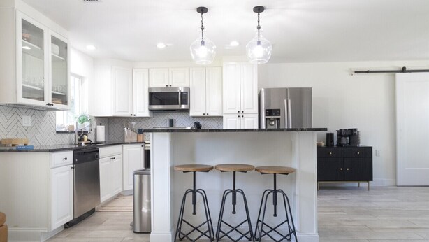 A modern kitchen with white cabinets, stainless steel appliances, and a central island with stools. - *NEW* Riverside Retreat w/ Pool (Jupiter)