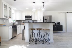A modern kitchen with white cabinets, stainless steel appliances, and a central island with stools. - *NEW* Riverside Retreat w/ Pool (Jupiter)