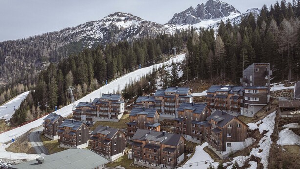 A cluster of wooden multi-story buildings with a ski lift in the background. - Superior Chalet With Finnish Sauna (Hermagor-Pressegger See)