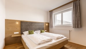 A bedroom with a wooden bed, a nightstand, a window with curtains, and a view of a snowy landscape. - Superior Chalet With Finnish Sauna (Hermagor-Pressegger See)
