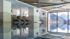Ein modernes Interieur mit Glasboden, Lounge-Stühlen und einem großen Fenster mit Blick auf die Berge.