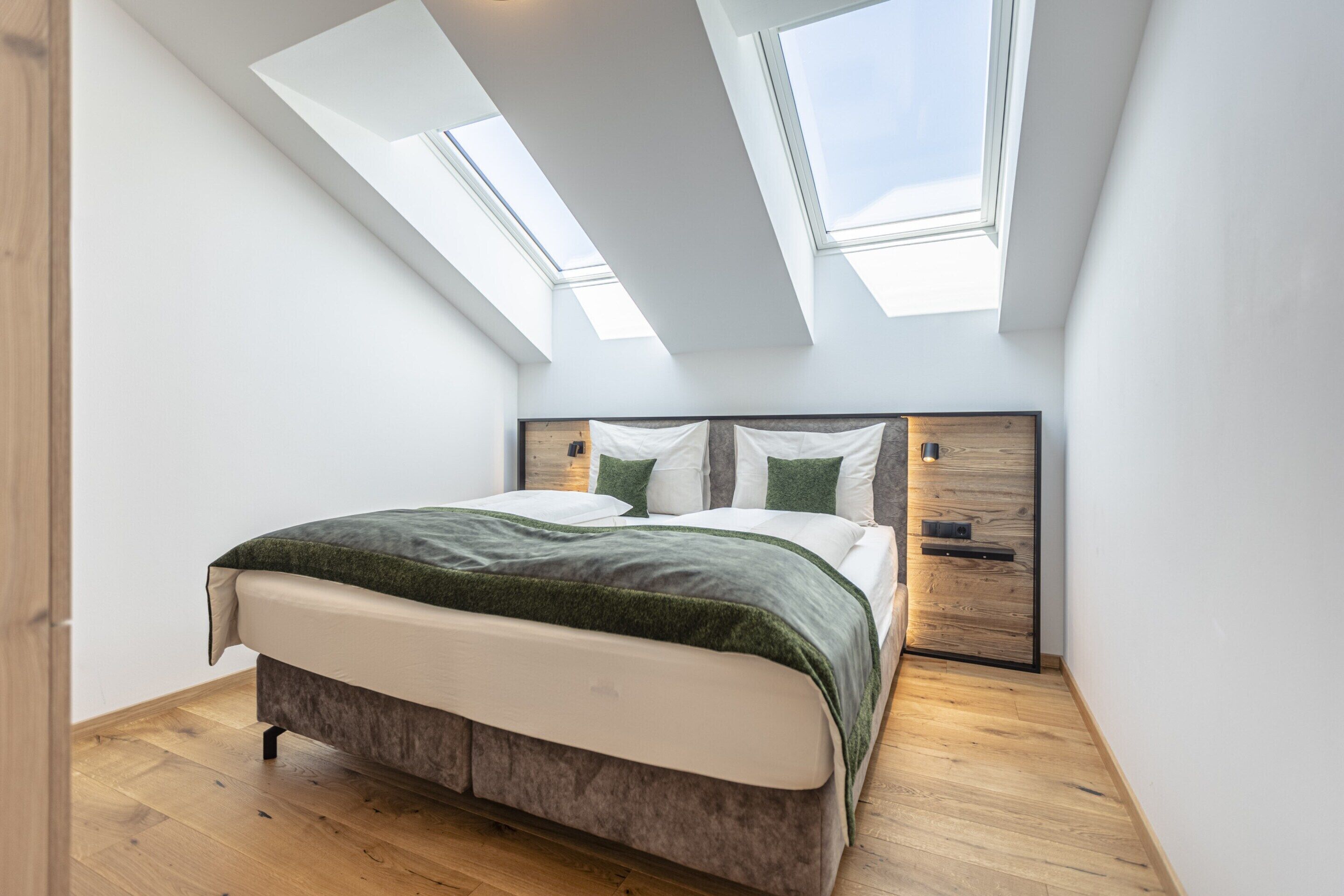 A bedroom with a bed, skylights, wooden flooring, and a nightstand.