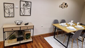 A dining area with a wooden table set for four, surrounded by grey chairs. There are two framed abstract artworks on the wall above the table. - AIOLOU st - 7th floor - 2 bdr, 80m2, most central apt - NetFlix - sleep 4p (Athina)