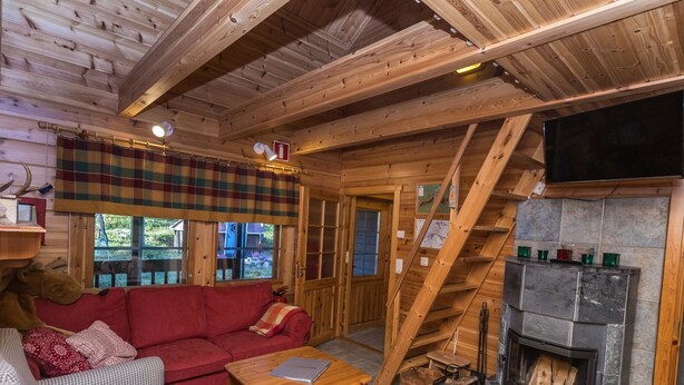Een gezellig chaletinterieur met een rode bank, een geruit fauteuil, een houten salontafel en een stenen open haard.