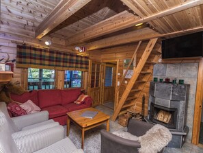 A cozy cabin interior with a red sofa, checkered sofa, and a fireplace.