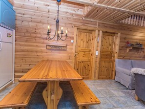 A wooden interior with a wooden table and benches, a refrigerator, and a sofa.