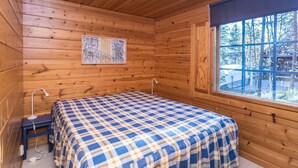 Een houten kamer met een bed, een raam en een plafondlamp.