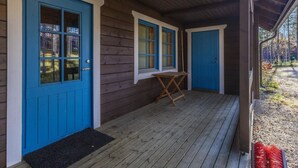 Een houten chalet met twee blauwe deuren, een kleine tafel en een overdekte veranda.