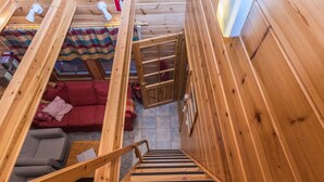 Een houten interieur met een trap die naar een lager gelegen niveau leidt, een rode bank en een gestreepte deken.