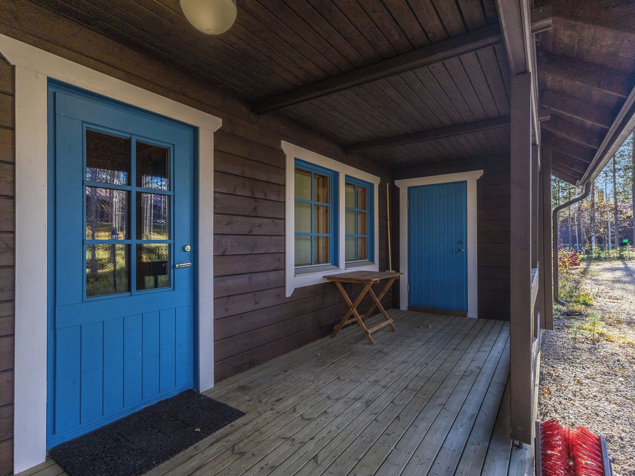 Un bâtiment en bois avec des portes et des fenêtres bleues, un porche couvert et une petite table.
