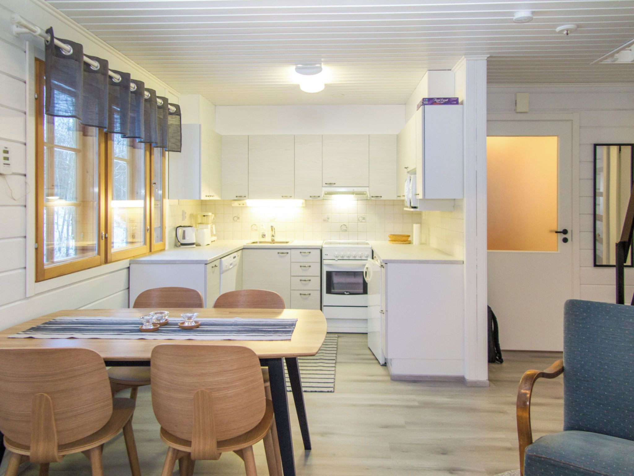 Kompakti keittiö, jossa on valkoiset kaapit, ruokapöytä tuoleineen ja pieni uuni.