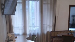 A room with a wooden desk, a chair, a glass table, a television mounted on the wall, and a window with curtains. - Comfortable apartment in delightful Beograd with WiFi, AC (Beograd)