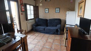 Un espacio habitable compacto con sofá, televisión, mesa de comedor y zona de cocina.