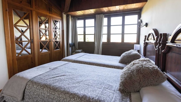 Habitación con dos camas, un armario de madera, ventanas amplias con cortinas y un cabecero de madera.