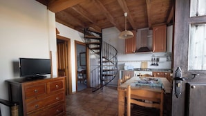 Una cocina compacta con una escalera de madera, un comedor con mesa y sillas, y un televisor sobre un aparador.