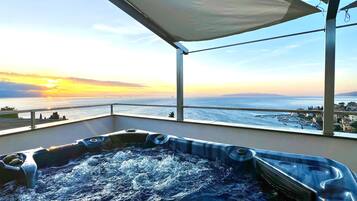 Un jacuzzi en un balcón con vistas al mar y al atardecer.