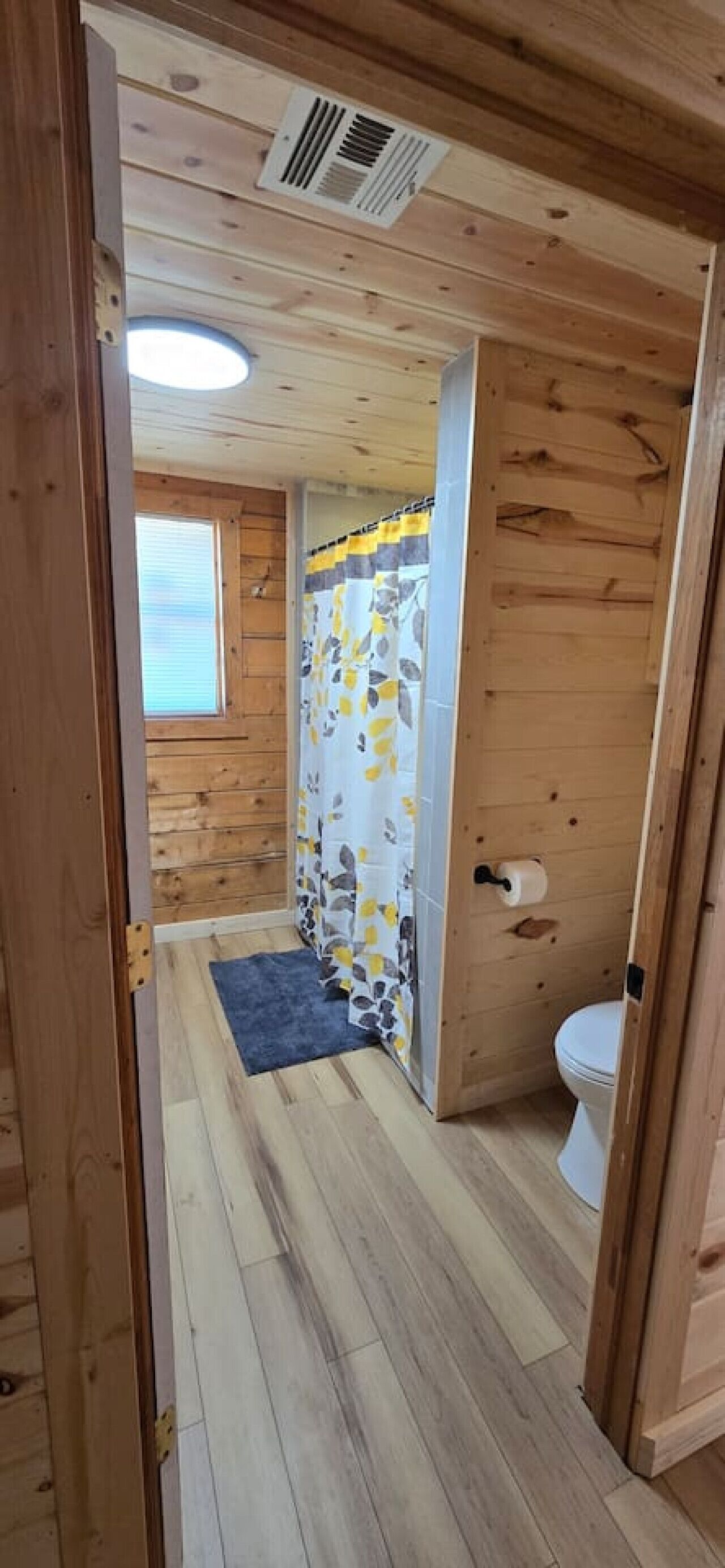 Et trægulv med et badeværelse, der indeholder toilet, brusekabine og et lille vindue.