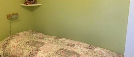A room with a single bed, a small shelf with a doll, and two framed pictures on the wall.