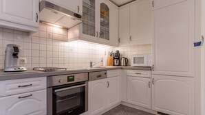 A modern kitchen with white cabinetry, a built-in oven, a coffee maker, and a microwave. - Ferienwohnung fur 3 in St. Peter-ording (St. Peter-Ording)