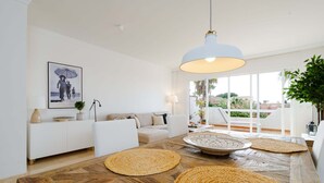Ein modernes Wohnzimmer mit einem Holzesstisch, weißen Sofas und einem großen Fenster mit Blick ins Freie.