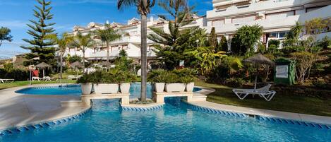 A swimming pool with a clear blue water feature, surrounded by lush greenery and white buildings with balconies.