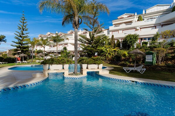 A swimming pool with a clear blue water feature, surrounded by lush greenery and white buildings with balconies. - Apartment Marbella 100m From Beach (Marbella)