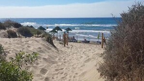 Ein sandiger Strand mit Sonnenschirmen und Liegestühlen, der zum Meer führt.
