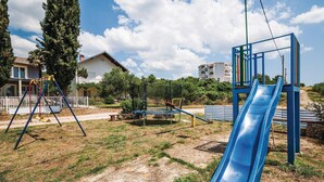 Un parque infantil con un tobogán azul, columpios y un trampolín.
