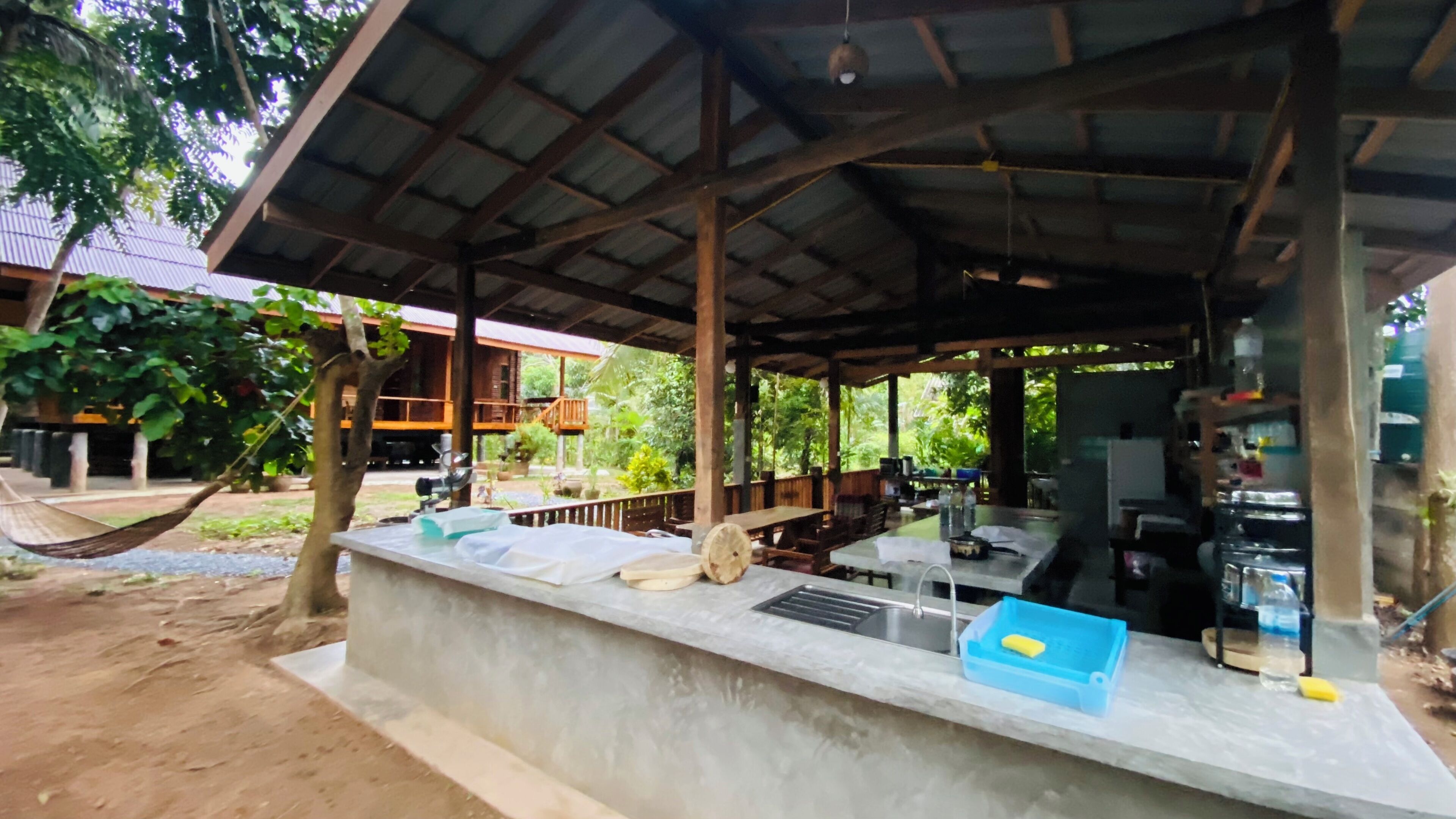 Un área de comedor al aire libre con techo, una barra de concreto, una hamaca y vista a un edificio con tejado rojo.
