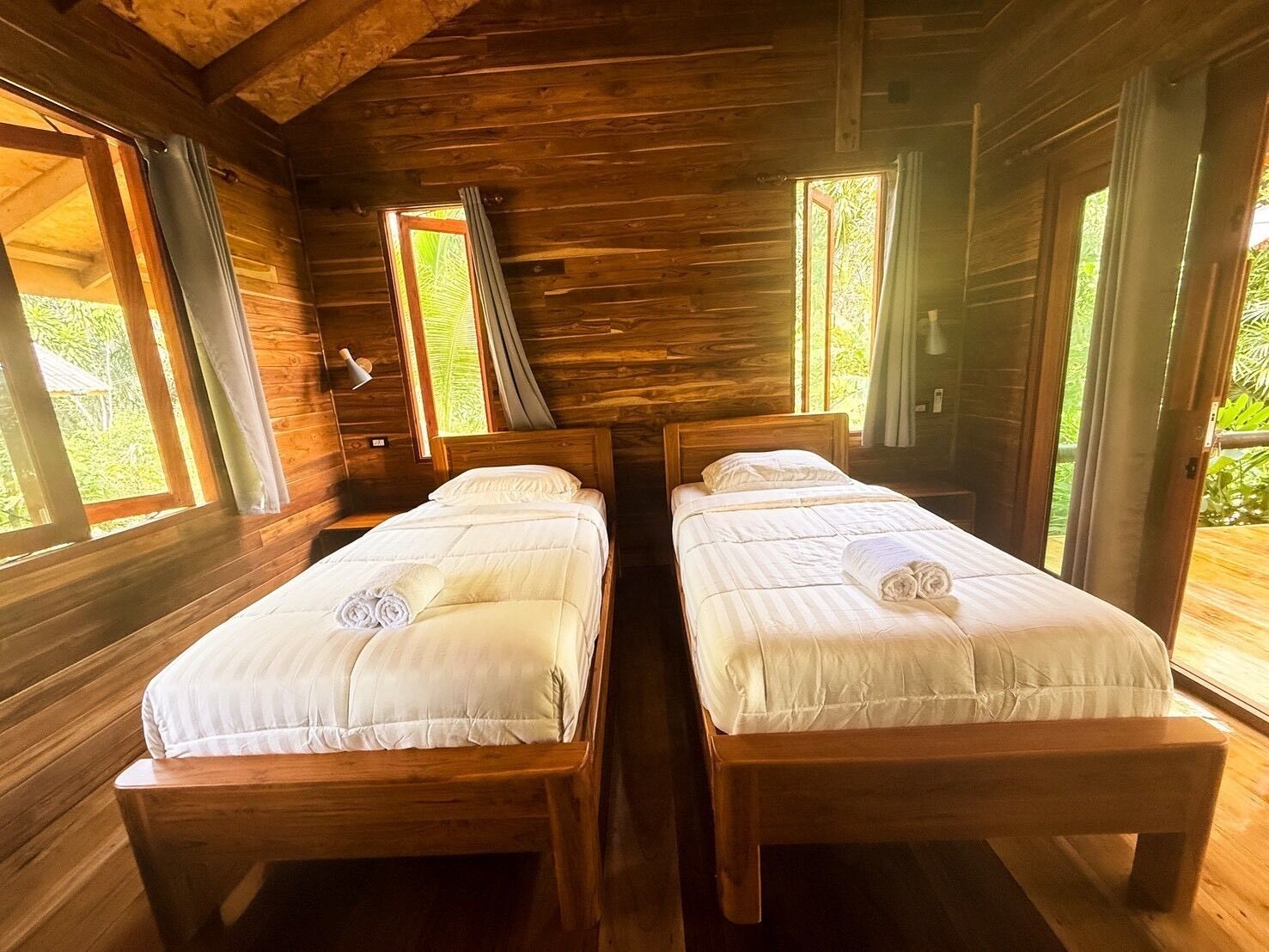 A cabin with two wooden beds, a wooden ceiling, and large windows.