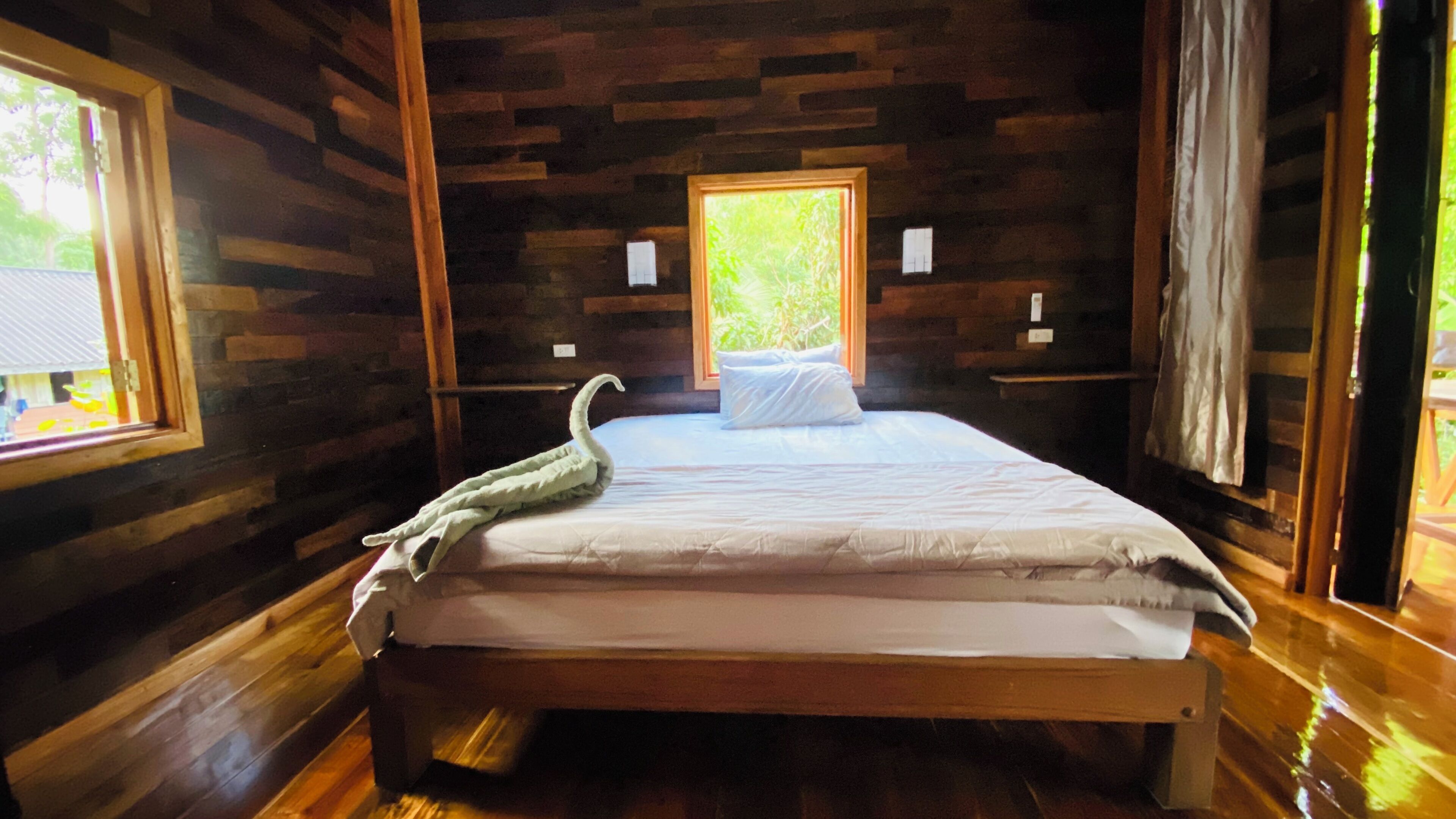Un dormitorio de cabaña de madera con cama, ventana y suelo de madera.