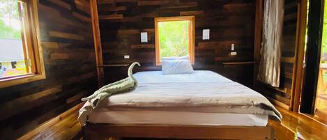 Un dormitorio de cabaña de madera con cama, ventana y suelo de madera.
