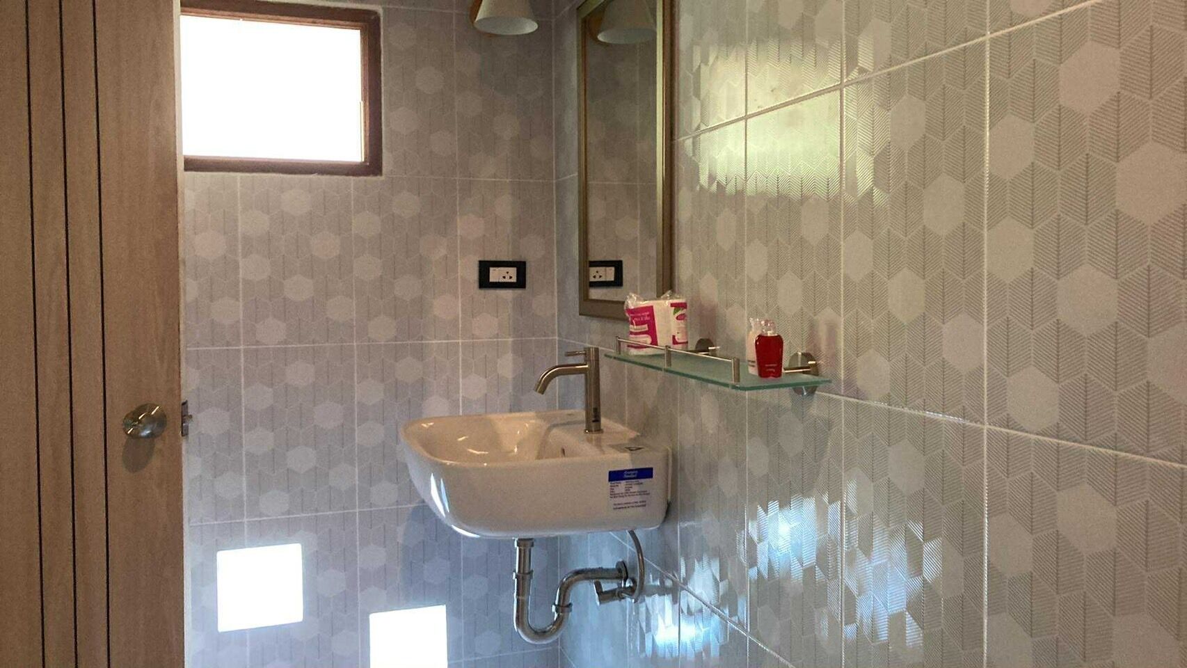 Een badkamer met een witte wastafel, een spiegel en een douchegedeelte. Er is een raam boven de wastafel en een douchegordijn zichtbaar.