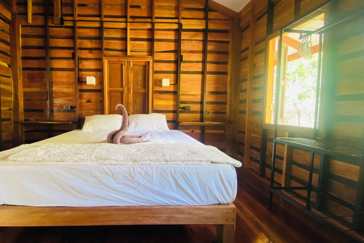 A wooden cabin-style room with a bed, a wooden bench, and a window.